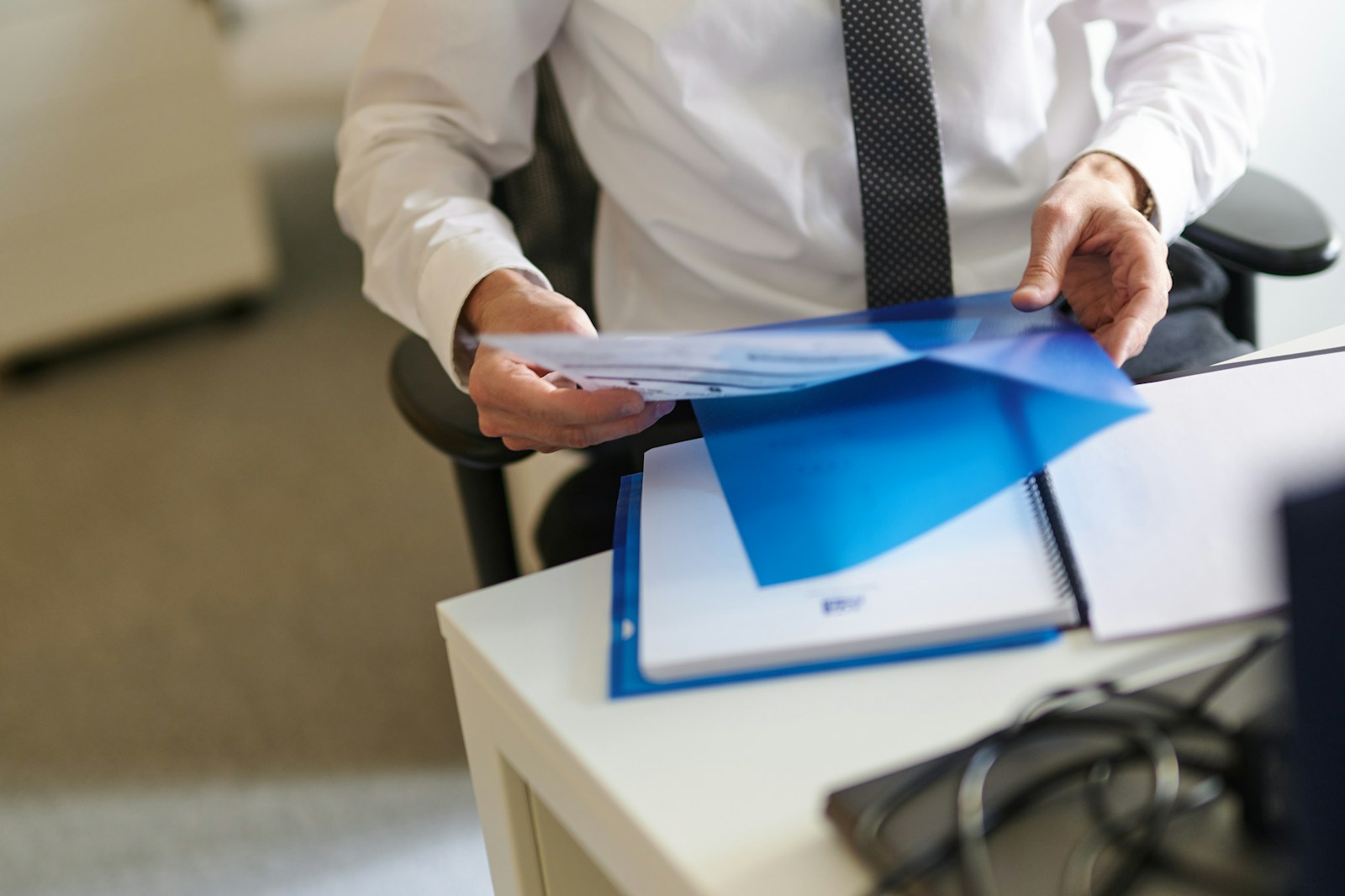 A man in a white shirt and tie holding a folder